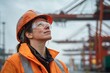 © Moritz - Smiling female industrial worker wearing safety gear at shipping port with cargo containers and cranes in background
