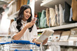 © Art_Photo - Asian woman shopping in home goods store smiling while pushing cart through bedding section, enjoying retail lifestyle, consumer behavior, weekend leisure, home decor at modern market
