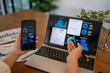© Apichat - person is using a laptop and a cell phone to view graphs and charts
