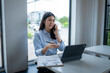 © Apichat - woman is talking on her cell phone while sitting at a desk with a laptop