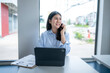 © Apichat - woman is talking on her cell phone while sitting at a desk with a laptop