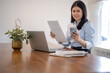 © Apichat - woman is sitting at a desk with a laptop and a cell phone