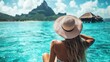 © An - A woman in a swimsuit sitting on a dock by the ocean, wearing a straw hat, with a mountain in the background.