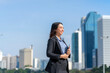 © StockPhotoRepublic - Smiling Asian businesswoman holding tablet with modern city skyline. Confident female professional outdoors in urban business district.