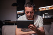 © Bits and Splits - Tired exhausted man reading social media content on digital tablet computer at home late at night