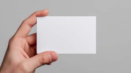 Wall Mural - A hand holds a blank white business card against a plain gray background.