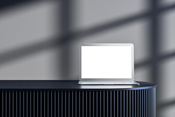 Laptop with blank screen placed on dark modern podium in stylish interior studio with soft shadow light pattern on background wall. 3D Rendering