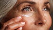 © PhotoLuxeStudio - Aging woman applying moisturizing cream on her face with visible wrinkles and natural skin texture in close up
