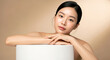 © minwoo Jung - 깨끗하고 빛나는 피부를 가진 아름다운 아시아 여성이 스킨케어 제품 디스플레이를 위해 흰색 받침대에 기대어 있는 이미지