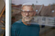© Westend61 - Man with glasses looking out a window in a loft, reflecting a serene and contemplative mood