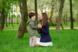 © khmelev - mother and son in park enjoying a tender moment surrounded by lush greenery. woman kneeling on grass holds boy’s hands with trees in background. happy family time in nature