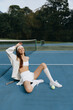 © SHOTPRIME STUDIO - Young athletic woman in sporty outfit enjoys tennis on the court, bright smile, with a tennis ball on the blue court surrounded by nature