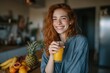 © Lady O - A young woman is holding a glass of orange juice in the kitchen at home, enjoying her morning breakfast and smiling while standing near a table with fruits.