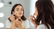 © luwie - Woman applying foundation makeup with brush in front of mirror for beauty and skincare routine tutorial