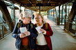© Davor - Senior women laughing and holding travel maps at train station platform