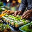 © Premium Resource - a vendor's hands preparing fresh Vietnamese spring rolls, translucent rice paper filled with shrimp and herbs, at a bustling street market, motion and authenticity