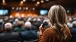 © Anna - Focused on a speaker holding a microphone, the audience is captivated, seated in a modern conference hall with warm lighting, creating a vibrant atmosphere during an engaging event
