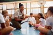 © Drazen - Happy black female coach with group of children during PE class at school gym.