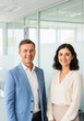 © InfinityVisuals - Confident Business Team: A smiling man and woman in business attire stand confidently together in a modern office setting.