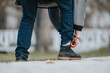 © qunica.com - A person outdoors adjusts their pants near the ankle while dressed in casual clothing and durable boots, symbolizing readiness and outdoor activity.