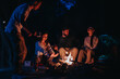 © qunica.com - A group of friends relaxing around a campfire in the evening, enjoying warmth and camaraderie in an outdoor setting beneath a dark, starry sky.