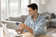 © fizkes - Digital payment confidence. Smiling young man provide online money transaction from credit card using banking app on notebook at home office to pay for digital service make purchase at ecommerce store