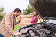 © Guillermo Spelucin - Frustrated couple checking broken down car engine on roadside