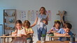 © stockbusters - Group children doing homework sitting class desks. Young woman teacher watching