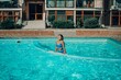 © svetograph - A woman is in the water, smiling and enjoying herself. The water is blue and the pool is surrounded by a white ledge.