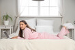 © Pixel-Shot - Young pretty woman in pajamas lying on bed and using laptop at home