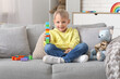 © Pixel-Shot - Happy cute little boy playing with colorful toy bricks and teddy bear on sofa at home