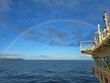© Lana Pietukhova - A vibrant rainbow arching over the blue ocean from the deck of a yellow ship under a partly cloudy sky, travel, maritime