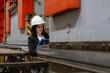 © Nassorn - Woman engineer manager working at steel production factory. Female inspector wears safety hard hat holding clipboard checking metal equipment and machinery maintenance in workshop. Quality control.