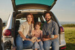 © Stockphotodirectors - Family relaxes in the back of a vehicle during a picturesque picnic, enjoying each other's company under a warm sunset sky while seated on the grass.