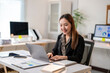 © Apichat - A woman is sitting at a desk with a laptop and a stack of papers