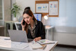 © Apichat - A woman is talking on her cell phone while sitting at a desk with a laptop
