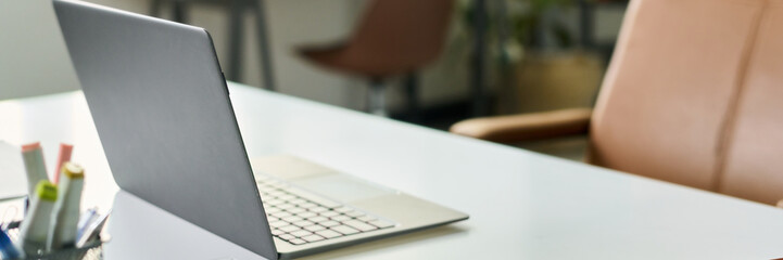 Open laptop standing on desk in modern office environment, workspace prepared for neural network development project, blurred background showing empty chair and office supplies
