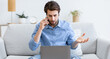 © Prostock-studio - Displeased Guy Talking On Cellphone Using Laptop, Having Computer Problem Sitting On Sofa At Home. Discontented Customer, Freelance And Remote Work Issue Concept. Selective Focus