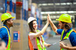 © Wanwajee - Warehouse workers in safety gear celebrating success with a high five. Smiling colleagues show teamwork, motivation, and achievement in a modern industrial work environment.