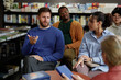 © Seventyfour - Caucasian middle aged man speaking during group discussion with Black middle aged man, Black young adult woman and Asian teenager listening in bookstore setting during session