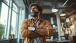 © svastix - A confident man with a distinctive beard and curly hair stands with crossed arms in a stylish modern workspace, radiating authority and assurance.