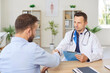 © Studio Romantic - Confident young male doctor therapist in white uniform shaking hands with a man patient sitting at the desk in office after medical examination in clinic. Medicine and health care concept.
