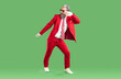 © Studio Romantic - Positive extravagant gray-haired Santa Claus dressed in classic stylish red suit. Studio photo of funny happy Santa Claus fooling around and dancing with his hand raised on isolated green background.