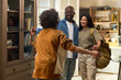 © pressmaster - Caucasian woman and Black man standing together smiling while welcoming curly haired child running toward them in home setting, military dog tag visible on woman, family reunion scene