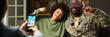 © pressmaster - Black middle aged man in military uniform sitting with smiling multiethnic child flexing arms while woman taking photo with smartphone at home, showing family bonding moment