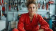© svastix - A skilled technician in a red work uniform sits confidently among tools in a workshop, representing dedication and expertise in her craft while maintaining a friendly demeanor.