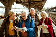 © Davor - Group of senior friends using smartphone for directions at train station