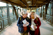 © Davor - Senior women laughing and holding travel maps at train station platform