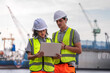 © ultramansk - Two engineers wearing safety vests and helmets inspect port operations near the waterfront. They use a laptop and walkie-talkie, symbolizing teamwork, logistics, and marine industry work.