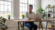 © Demas - Young Professional Woman Smiling Sitting at Desk with Laptop and Coffee in Bright Office Surrounded by Plants